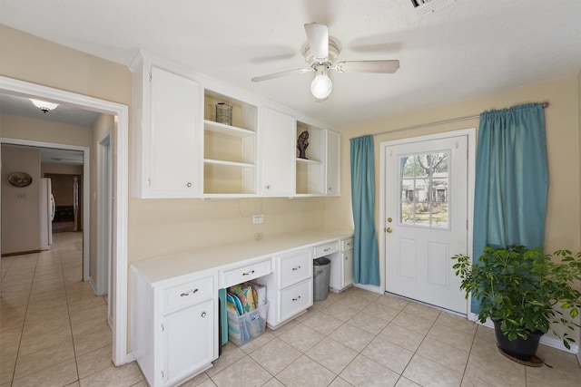 office featuring built in desk, light tile patterned floors, visible vents, ceiling fan, and baseboards