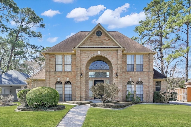 georgian-style home with brick siding, roof with shingles, and a front yard