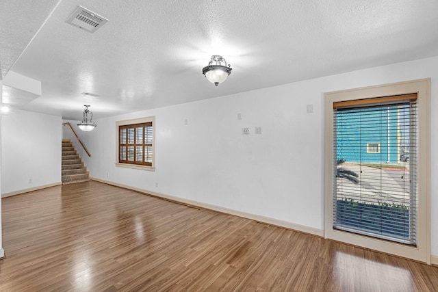 empty room featuring stairs, a textured ceiling, wood finished floors, and visible vents