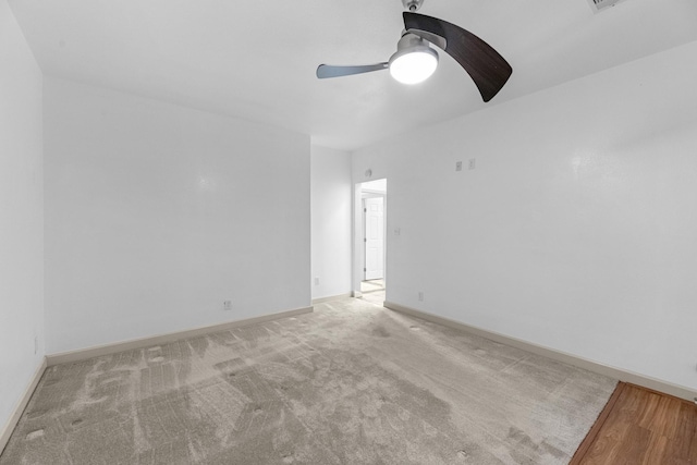 empty room featuring a ceiling fan, light colored carpet, and baseboards