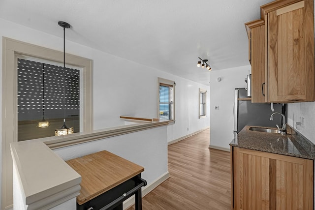 kitchen featuring light wood-style flooring, a sink, baseboards, brown cabinets, and dark stone counters