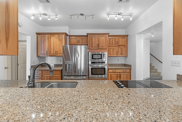 kitchen featuring light stone countertops, appliances with stainless steel finishes, brown cabinetry, and a sink