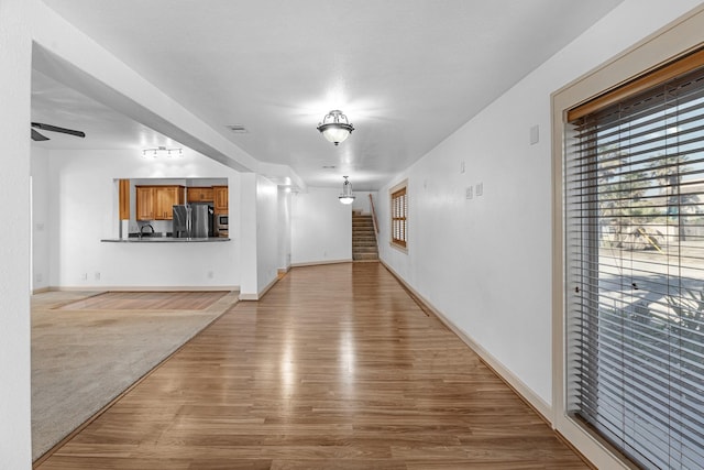 unfurnished living room with visible vents, baseboards, ceiling fan, stairway, and wood finished floors