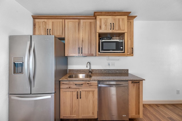 kitchen featuring stainless steel appliances, wood finished floors, a sink, baseboards, and dark stone counters