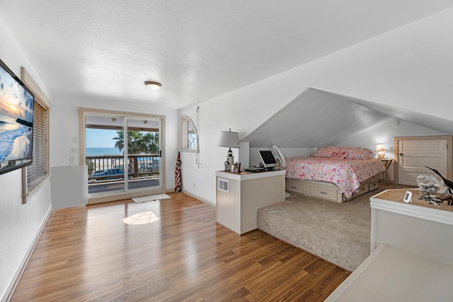 bedroom with access to exterior, vaulted ceiling, a textured ceiling, and wood finished floors