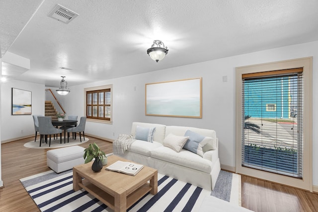 living room with a textured ceiling, stairway, wood finished floors, and visible vents