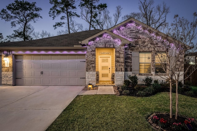 view of front of house featuring an attached garage, a shingled roof, stone siding, driveway, and a front yard