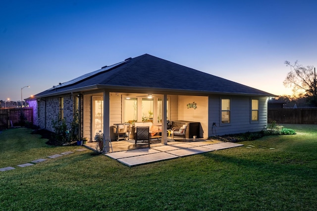 back of house at dusk featuring roof with shingles, a lawn, a patio area, and fence