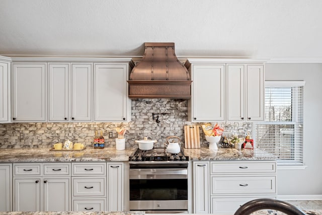 kitchen featuring light stone counters, tasteful backsplash, white cabinets, gas range, and custom exhaust hood