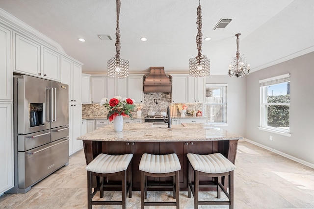 kitchen featuring visible vents, premium range hood, decorative backsplash, hanging light fixtures, and stainless steel refrigerator with ice dispenser