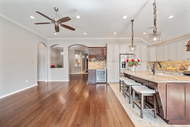 kitchen with crown molding, light stone countertops, wine cooler, stainless steel refrigerator with ice dispenser, and a sink