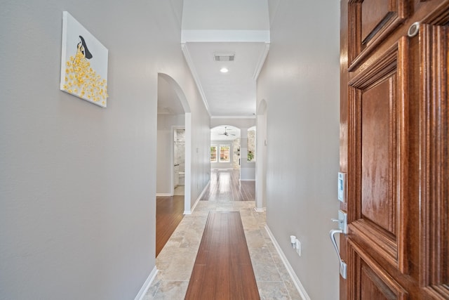 hall with visible vents, baseboards, arched walkways, and ornamental molding