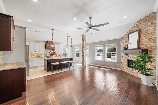 kitchen featuring visible vents, freestanding refrigerator, a stone fireplace, a breakfast bar area, and custom exhaust hood