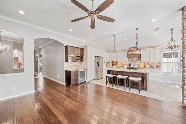 kitchen featuring a center island with sink, high end fridge, wine cooler, light wood-style floors, and a kitchen bar