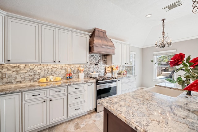 kitchen with visible vents, premium range hood, stainless steel range with gas cooktop, lofted ceiling, and a sink