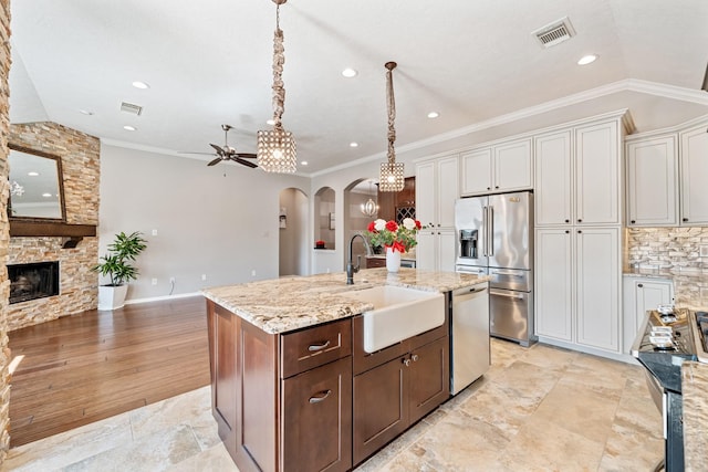 kitchen featuring visible vents, a stone fireplace, arched walkways, stainless steel appliances, and a sink