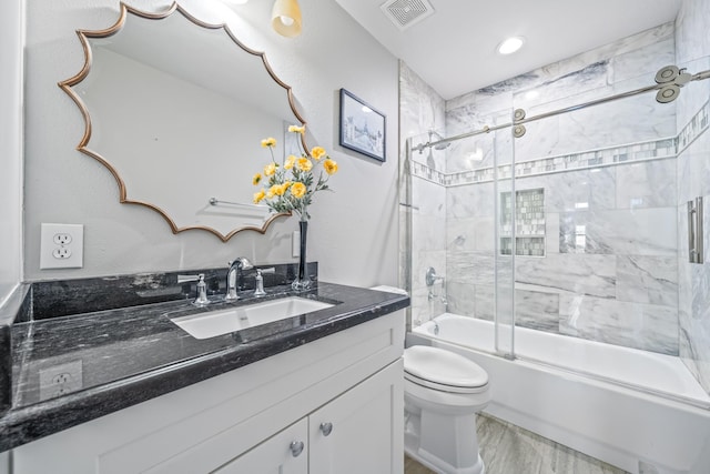 bathroom featuring visible vents, toilet, wood finished floors, enclosed tub / shower combo, and vanity