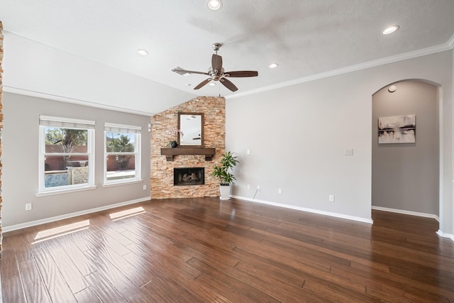 unfurnished living room with wood finished floors, baseboards, lofted ceiling, arched walkways, and a stone fireplace