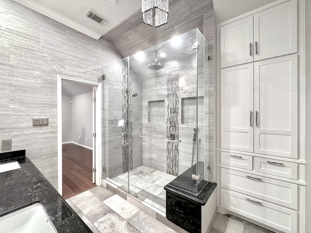 full bath with visible vents, a stall shower, a sink, wood finished floors, and tile walls