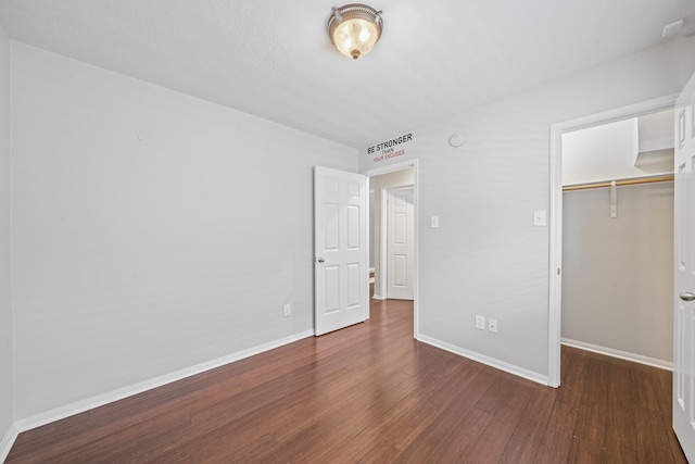 unfurnished bedroom with a closet, a walk in closet, baseboards, and wood finished floors