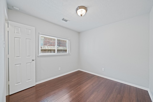 empty room with visible vents, a textured ceiling, baseboards, and wood finished floors