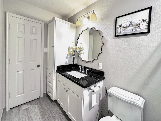 half bath featuring toilet, vanity, a textured wall, wood finished floors, and a textured ceiling