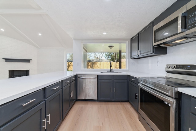 kitchen with stainless steel appliances, a sink, vaulted ceiling, light countertops, and light wood finished floors