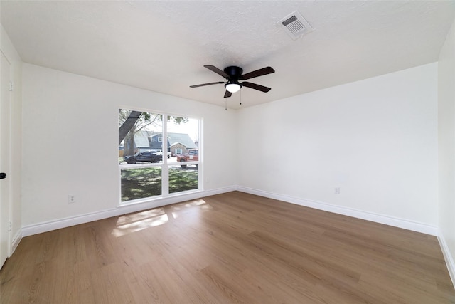 empty room featuring a textured ceiling, wood finished floors, a ceiling fan, visible vents, and baseboards