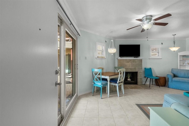 living room featuring light tile patterned floors, a tile fireplace, a ceiling fan, baseboards, and ornamental molding