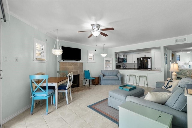 living area featuring light tile patterned floors, visible vents, a tiled fireplace, ceiling fan, and crown molding