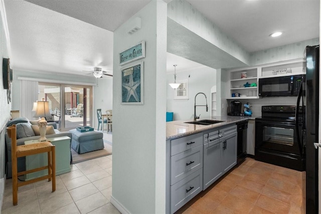 kitchen with gray cabinetry, open floor plan, a sink, light stone countertops, and black appliances