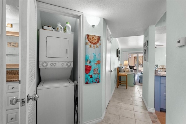 laundry room with laundry area, baseboards, stacked washer / drying machine, a textured ceiling, and light tile patterned flooring