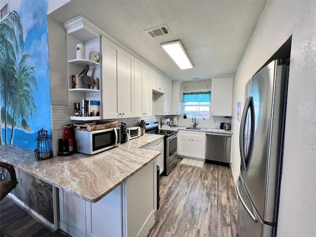 kitchen with open shelves, appliances with stainless steel finishes, white cabinetry, a sink, and a peninsula