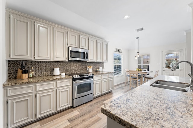 kitchen featuring visible vents, a sink, stainless steel appliances, light wood-style floors, and tasteful backsplash