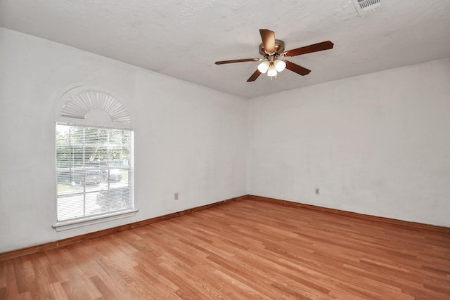 spare room featuring a textured ceiling, a ceiling fan, baseboards, visible vents, and light wood-style floors