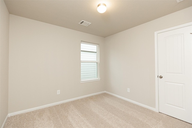 spare room with light colored carpet, visible vents, baseboards, and a textured ceiling