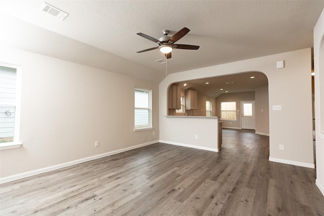 unfurnished living room featuring dark wood-type flooring, arched walkways, a healthy amount of sunlight, and visible vents