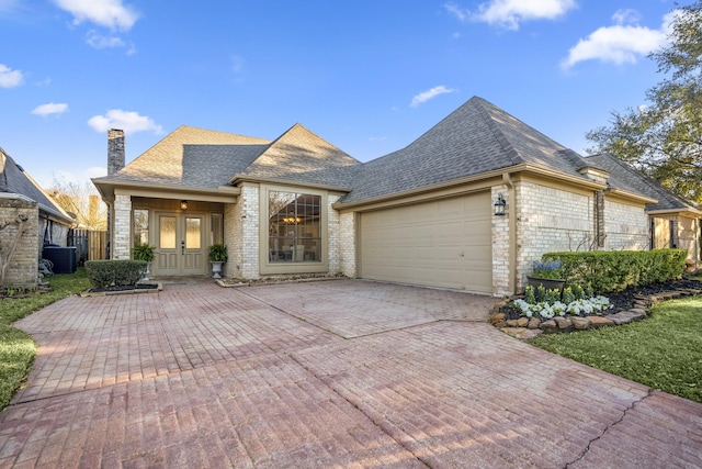 french country style house featuring a garage, a shingled roof, a chimney, decorative driveway, and french doors