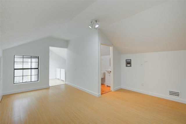 additional living space with light wood-style floors, visible vents, vaulted ceiling, and baseboards