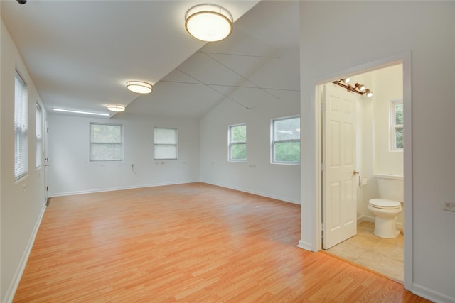 spare room featuring light wood-style floors, lofted ceiling, and baseboards