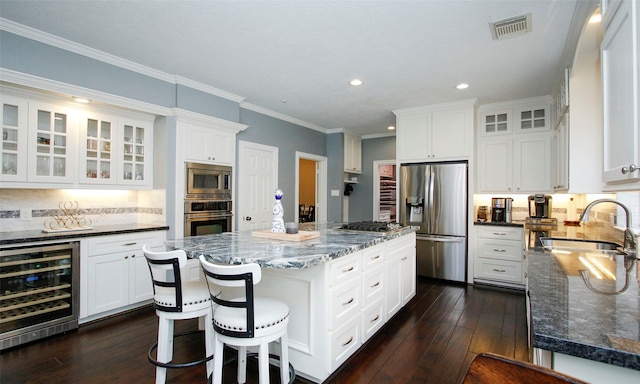 kitchen with beverage cooler, visible vents, a kitchen island, appliances with stainless steel finishes, and a sink