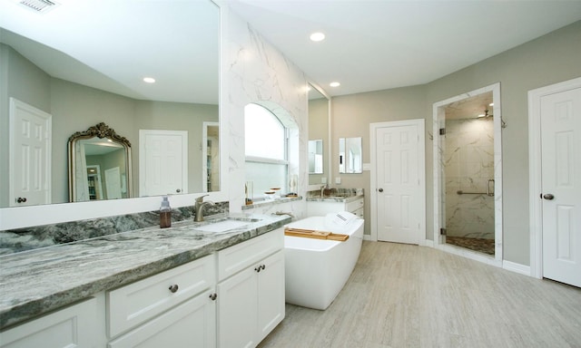 full bath with a freestanding bath, a marble finish shower, vanity, and recessed lighting