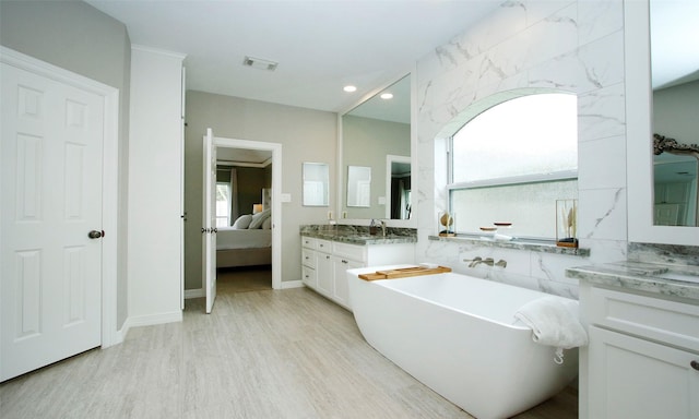 ensuite bathroom featuring visible vents, ensuite bathroom, a sink, wood finished floors, and a freestanding tub