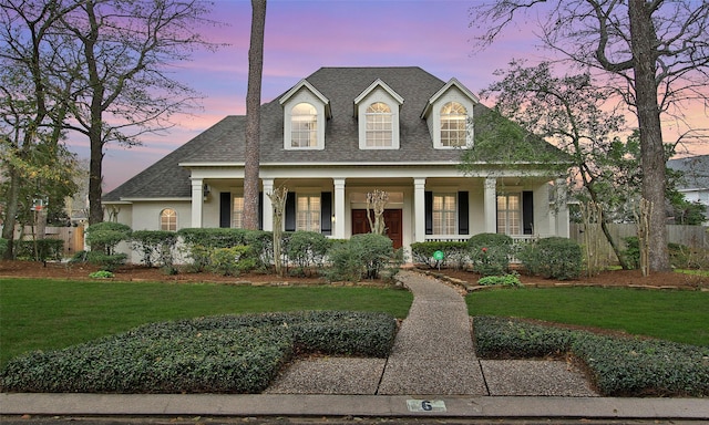 view of front facade with covered porch, fence, a front lawn, and roof with shingles