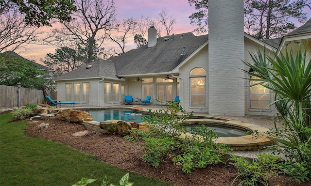 rear view of house with a chimney, a ceiling fan, a patio area, fence, and an in ground hot tub