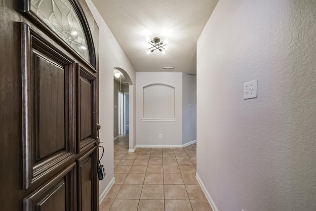 interior space with arched walkways, visible vents, a textured wall, light tile patterned flooring, and baseboards