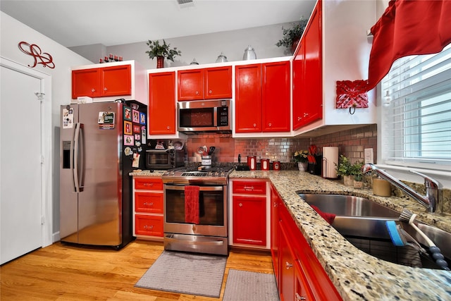 kitchen featuring light wood finished floors, stainless steel appliances, tasteful backsplash, red cabinetry, and a sink