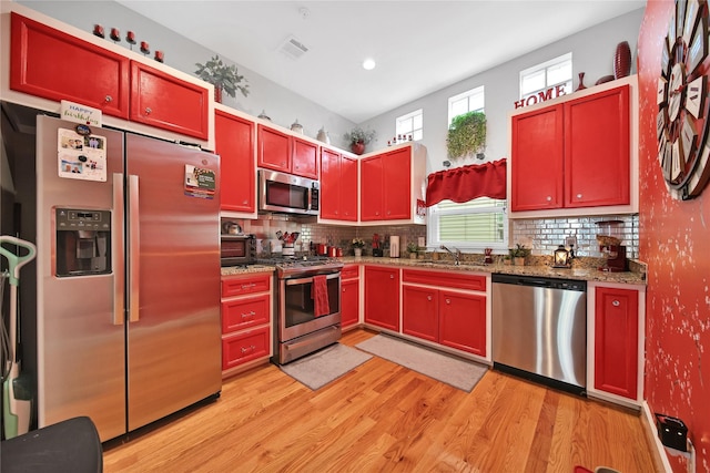 kitchen with appliances with stainless steel finishes, a sink, dark brown cabinets, light wood-type flooring, and backsplash