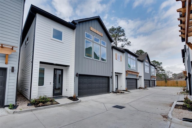 multi unit property with board and batten siding, concrete driveway, fence, and an attached garage