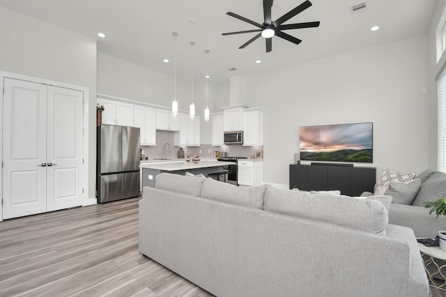 living area with light wood finished floors, recessed lighting, visible vents, a towering ceiling, and ceiling fan